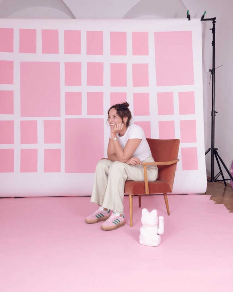 Frau sitzt in einem Studio mit pinkem Hintergrund, bereit für Rednertraining.